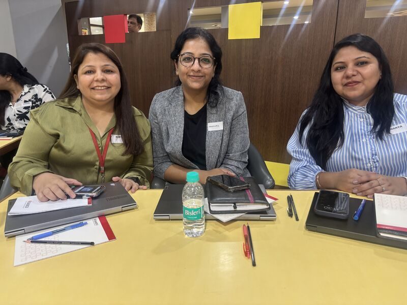 Three Damco delivery leaders at a workshop table with notes and laptops