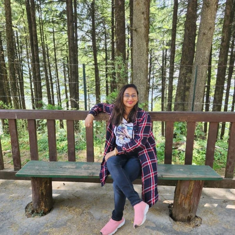 Akanksha Rastogi on a bench in a pine forest